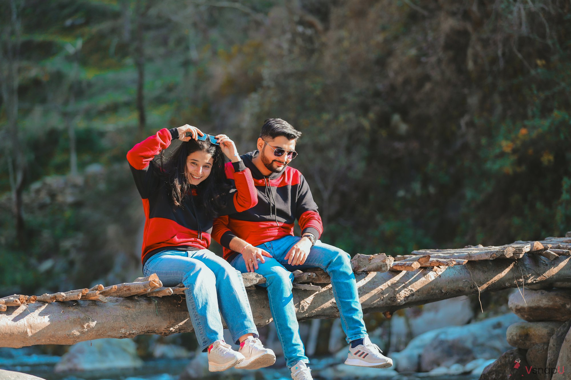 Pre-wedding couple sitting together on a river pier, bundled up in matching clothing amidst a snowy setting.